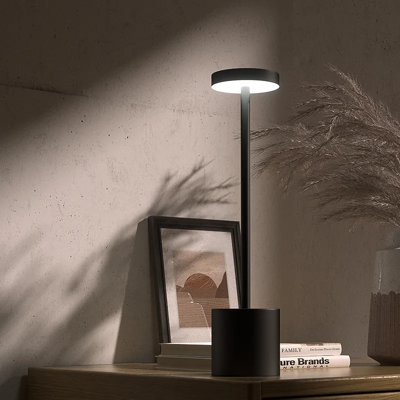 Modern black table lamp on a wooden surface with a framed picture and books in the background.