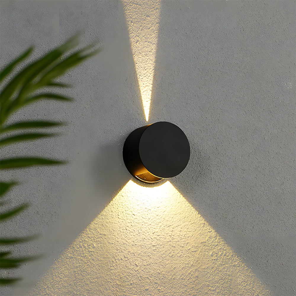 Modern black wall light fixture casting a shadow on a textured wall with a plant leaf in the corner.