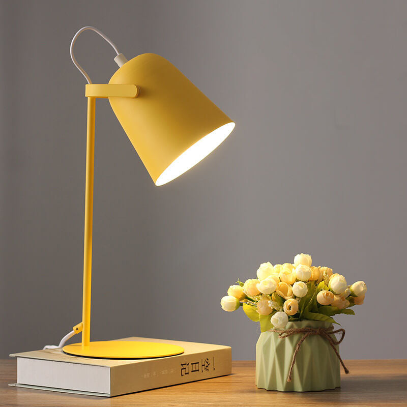 Yellow desk lamp on a book with a small potted plant on a wooden surface against a gray background