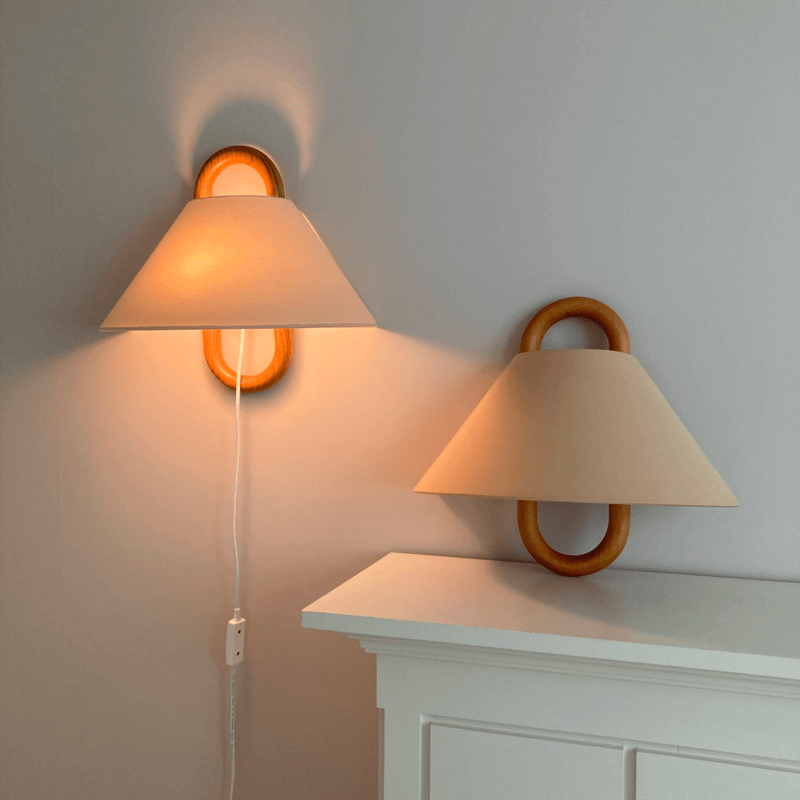 Two wall-mounted lamps with beige shades on a light gray wall.
