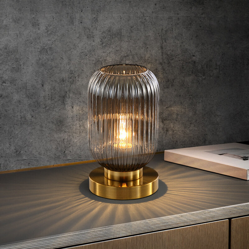 Table lamp with ribbed glass shade and gold base on a wooden surface with a concrete wall background
