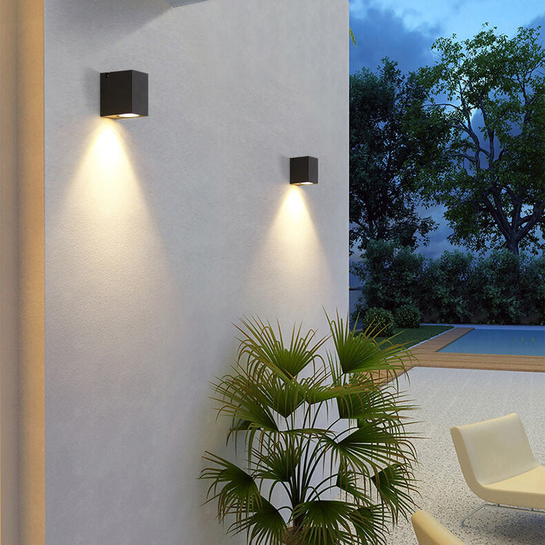 Outdoor wall lights on a building exterior with a garden and pool area in the background.