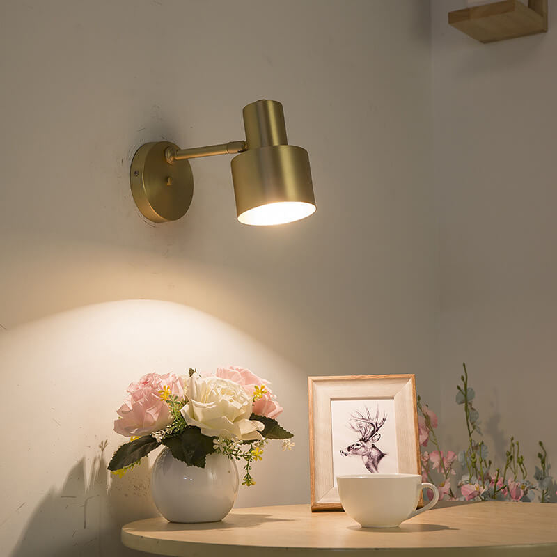 Gold wall lamp on a wall with a table below featuring a vase of flowers and a mug.