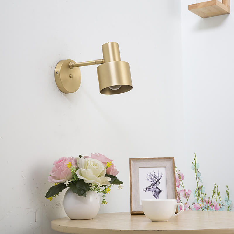 Gold wall lamp on a white wall with decorative items on a shelf.