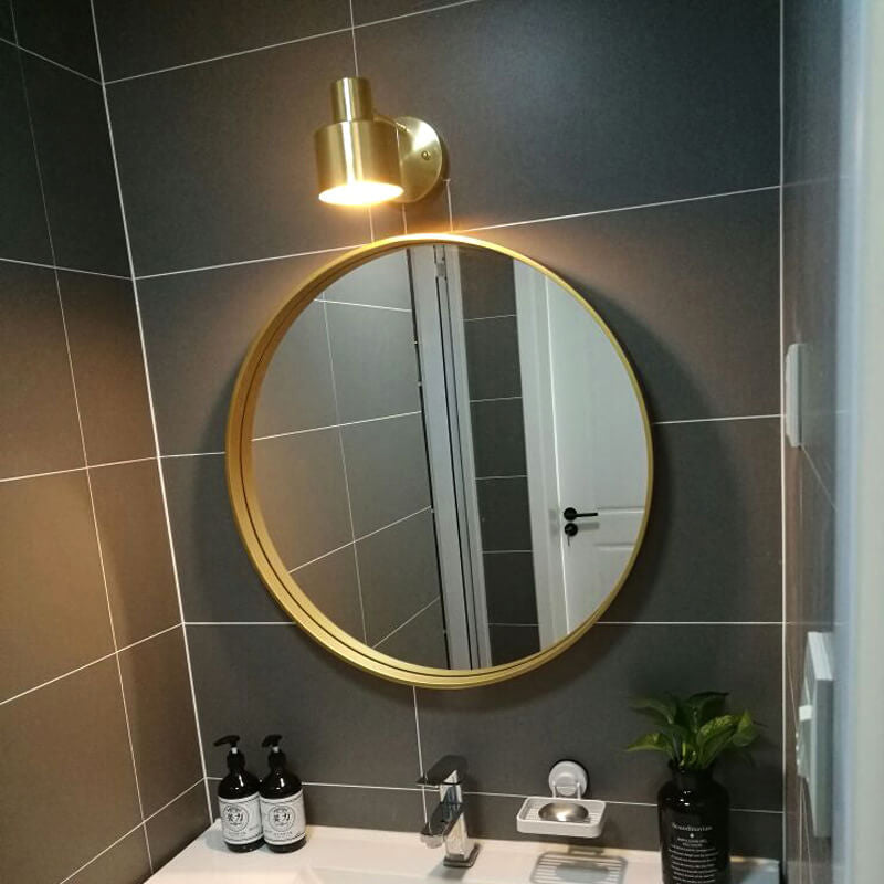 Round gold-framed mirror on a tiled wall with a light fixture above