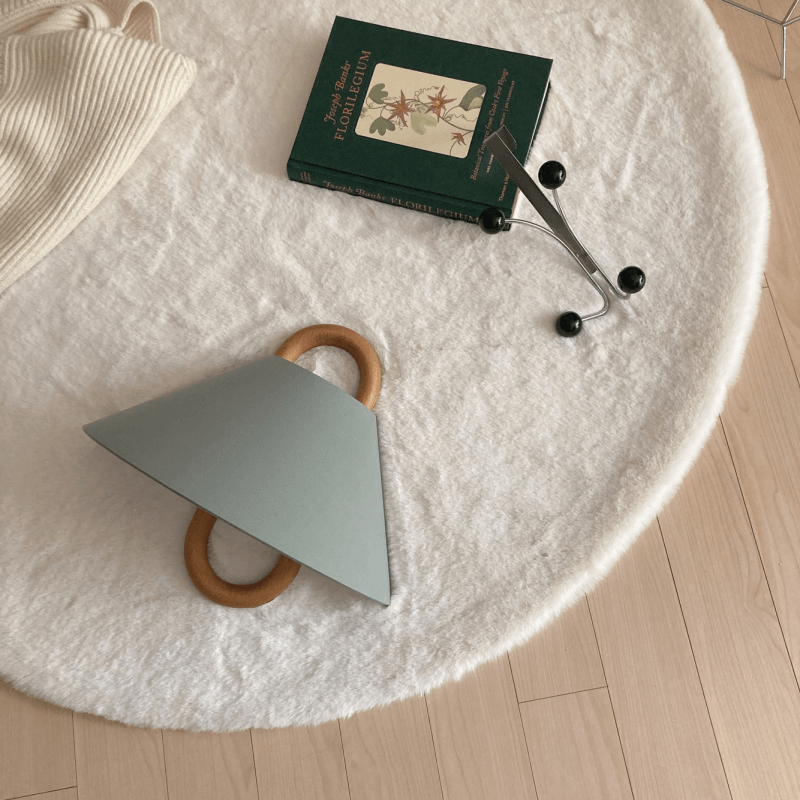 Round white table with a green geometric object, book, and black items on a light wooden floor.