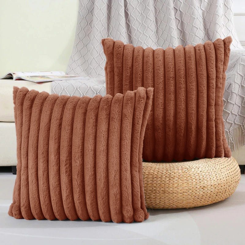 Two brown textured pillows on a white surface with a light gray textured wall in the background.