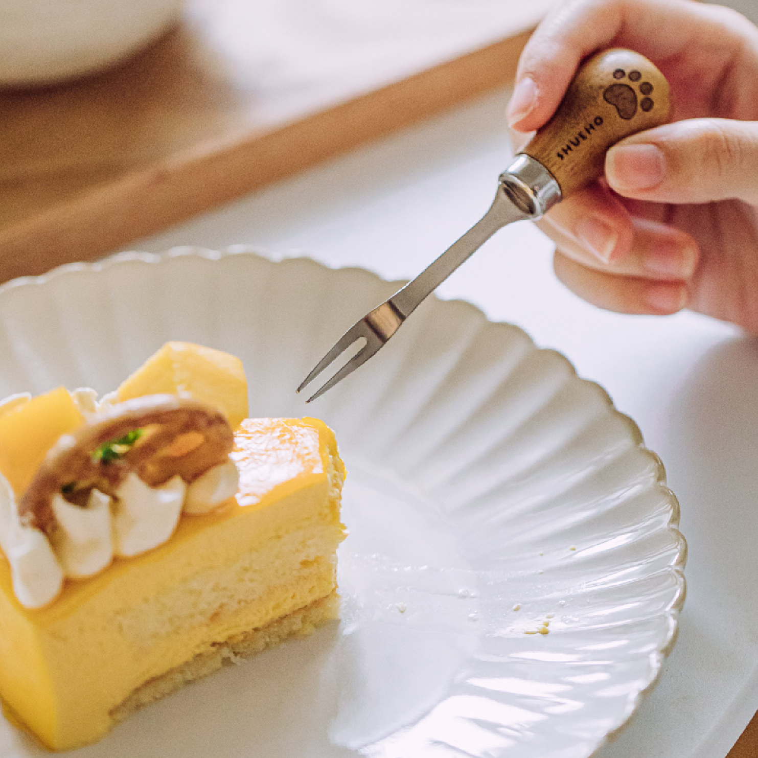 Slice of yellow cake with white frosting on a white plate, being cut with a decorative fork.