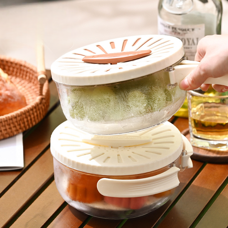 Two stacked salad spinners on a wooden table with a glass of juice and bottle in the background.