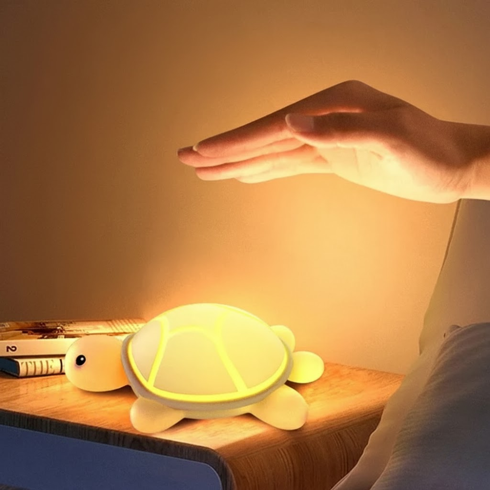 Tortoise-shaped night light on a desk with a hand reaching out to touch it.