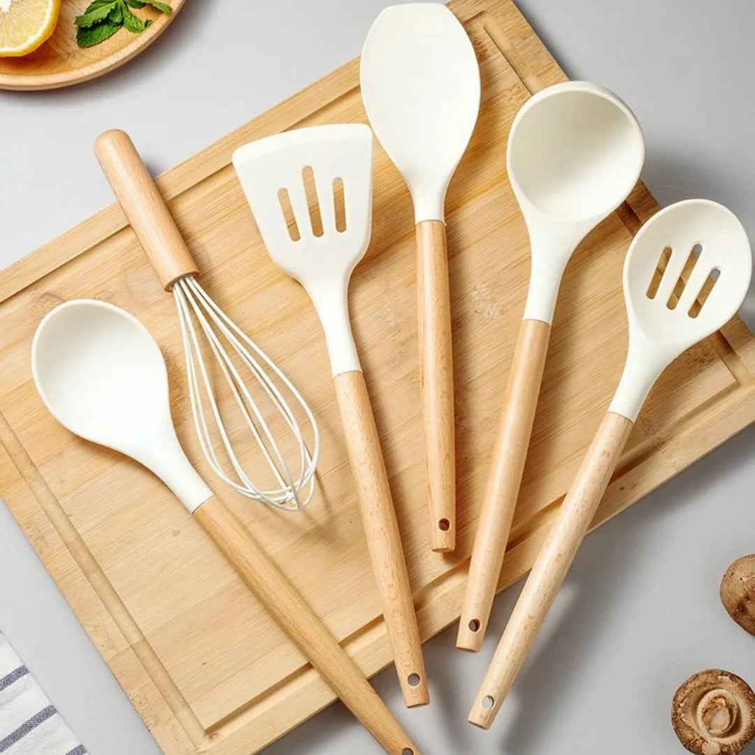 Set of kitchen utensils including spoons, spatulas, and a whisk on a wooden cutting board.