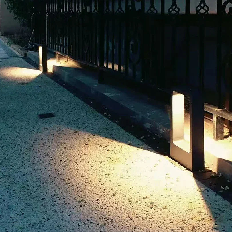 Outdoor pathway with illuminated ground lights casting shadows on a gravel surface.
