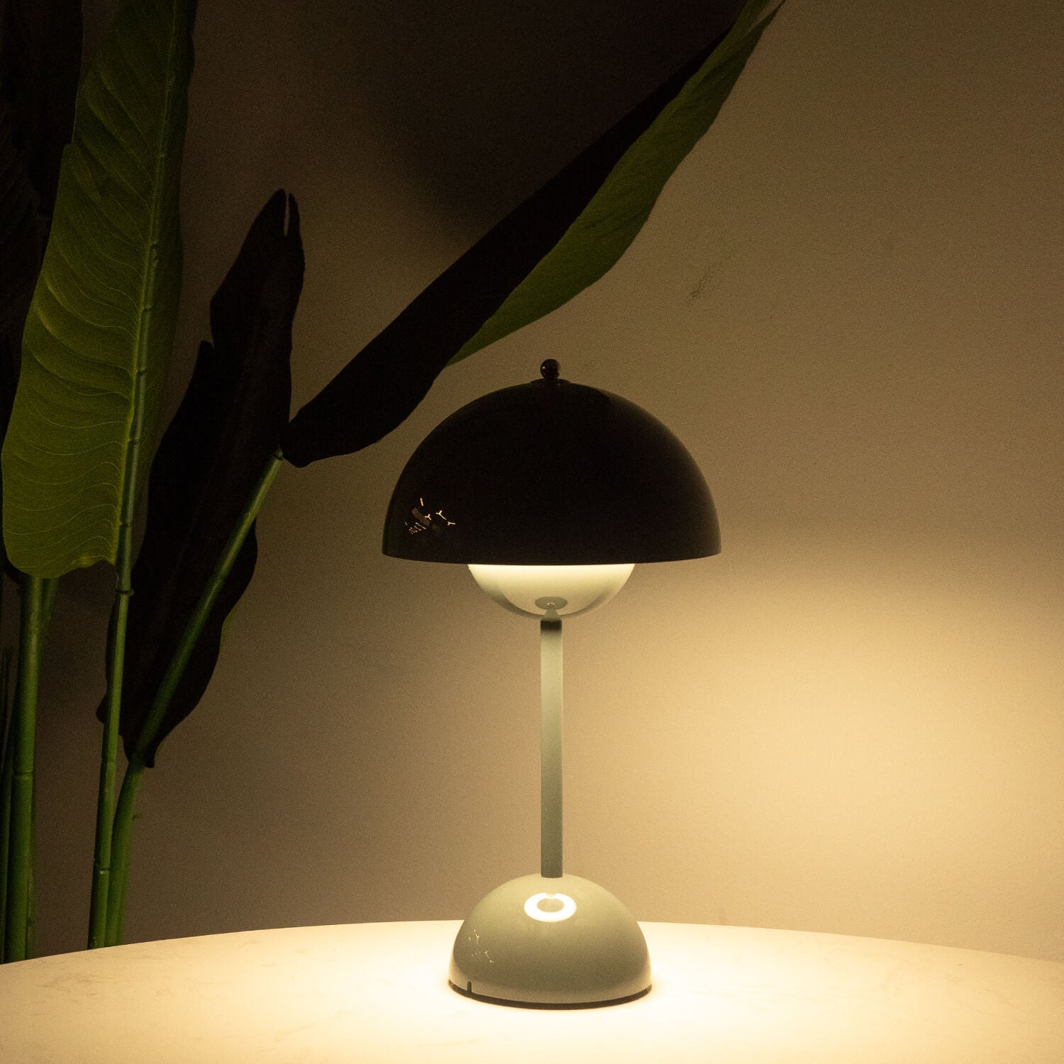 Table lamp with a black shade and white base on a surface, illuminated against a dark background.