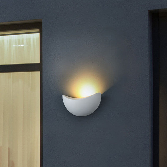 White wall-mounted light fixture on a dark blue wall with a window to the left.