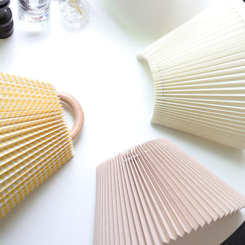 Three pleated bags in yellow, beige, and white on a light surface.