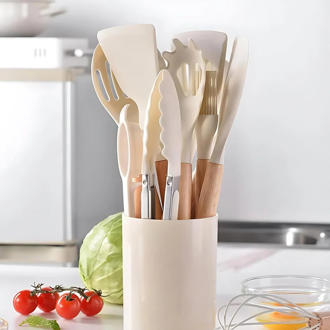 Set of kitchen utensils in a white holder on a kitchen counter with vegetables and a whisk.