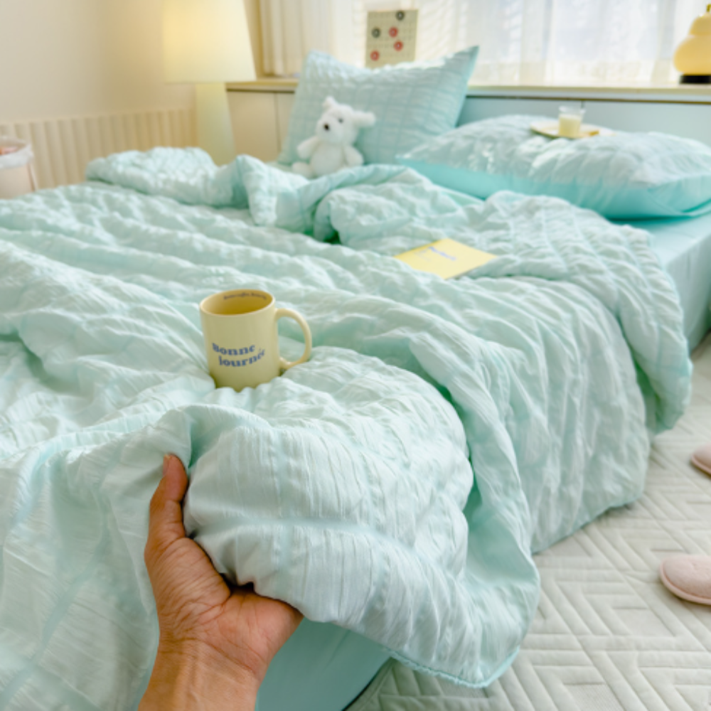 Light blue textured comforter on a bed with a hand holding it, in a bedroom setting.