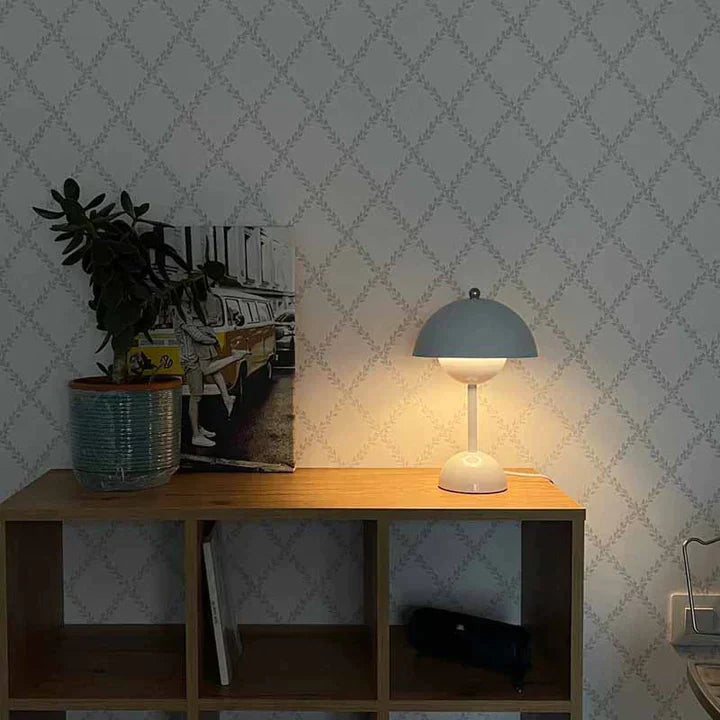 Wooden shelf with a lamp, plant, and photo against a patterned wall.