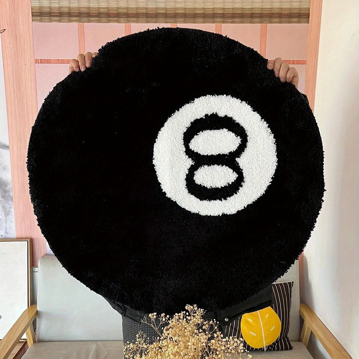Round black pillow with a white number 8 design held by a person indoors.