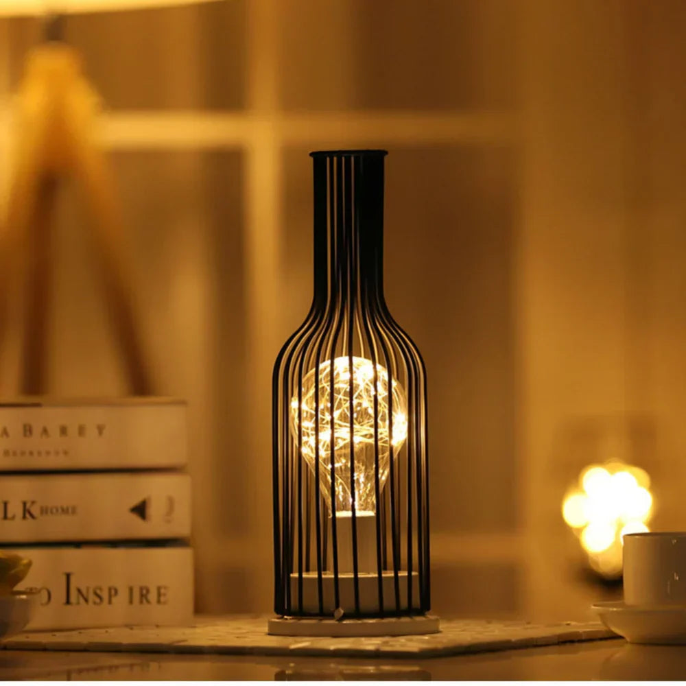 Decorative bottle-shaped lamp with a glowing light bulb inside, placed on a surface with books and a blurred background.
