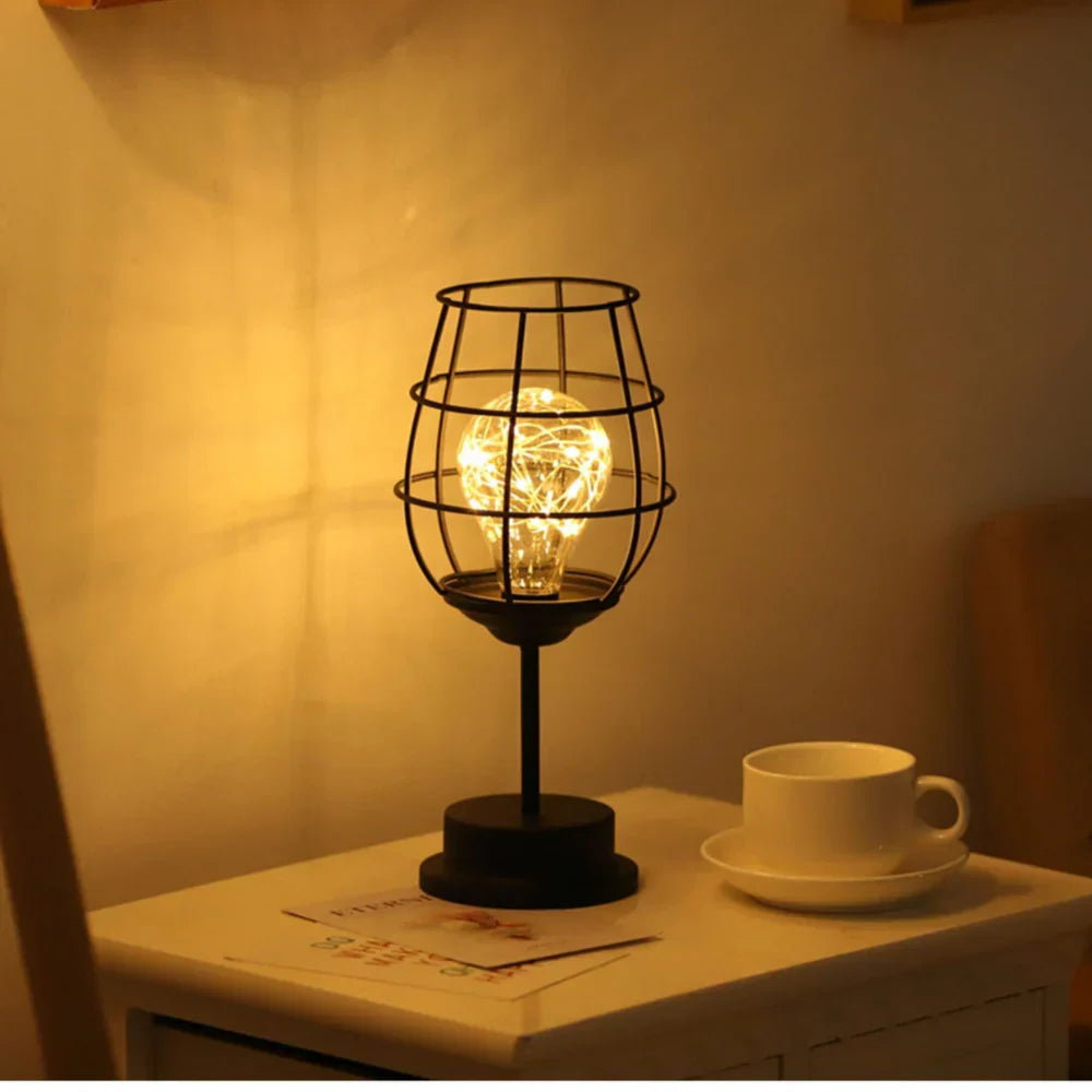 Decorative table lamp with a wire cage design on a surface with a cup and saucer.