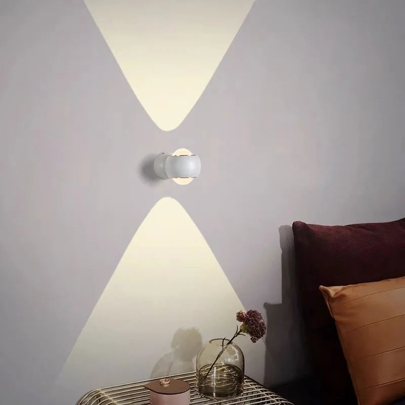 Modern wall light fixture casting a warm glow on a wall with decorative pillows and a vase.