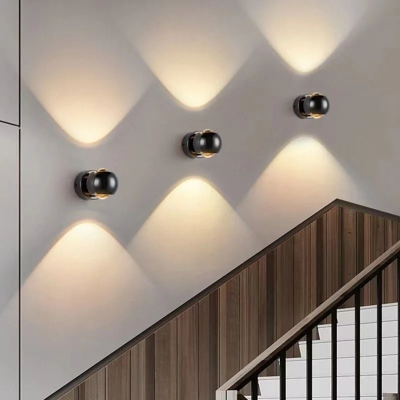 Modern wall lights on a staircase with wooden railings and white walls.