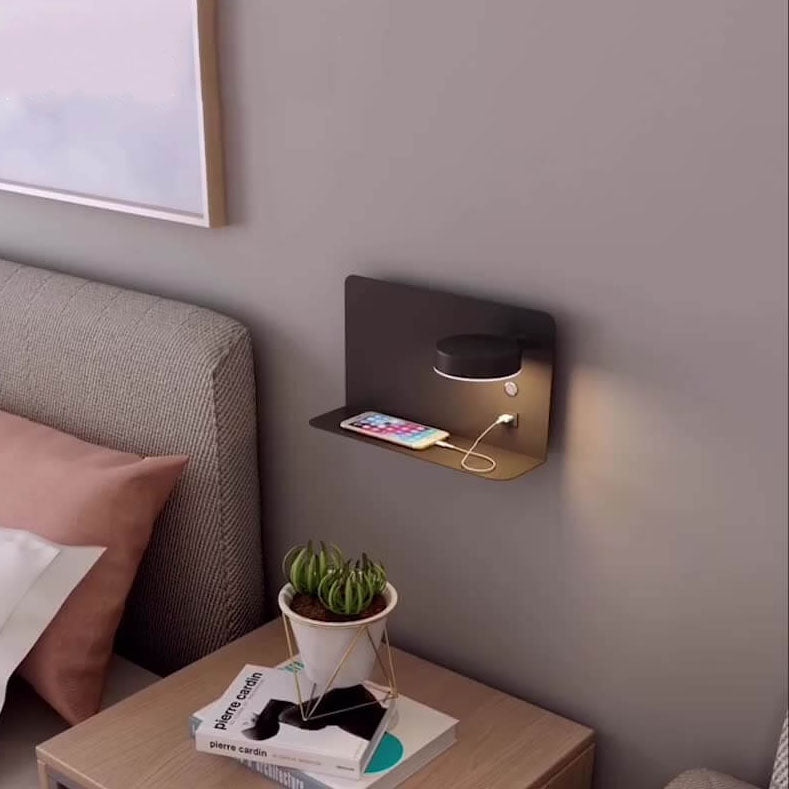 Wall-mounted charging station with a phone and lamp on a bedside table.
