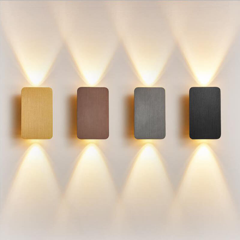 Four rectangular wall lights in gold, bronze, gray, and black on a white wall.