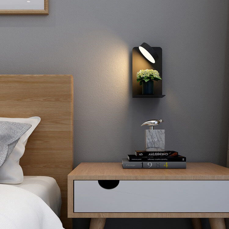 Modern bedroom with wooden headboard and nightstand, wall lamp, and books.