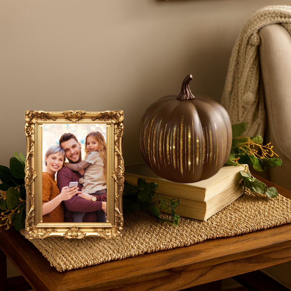 Decorative setup with a gold-framed photo of a family, a bronze pumpkin, and books on a wooden surface.