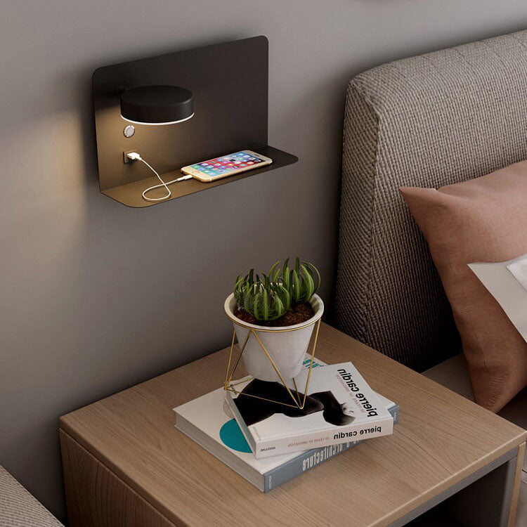 Wall-mounted night light with charging port on a bedside table next to a bed.