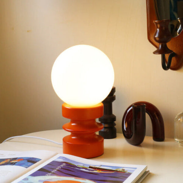 Table lamp with a round white bulb on an orange base, placed on a surface with books and decorative items.