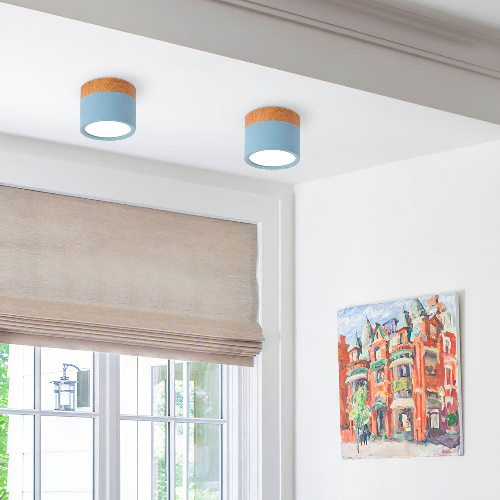 Two ceiling lights with blue shades and wooden accents in a room with a window and artwork.