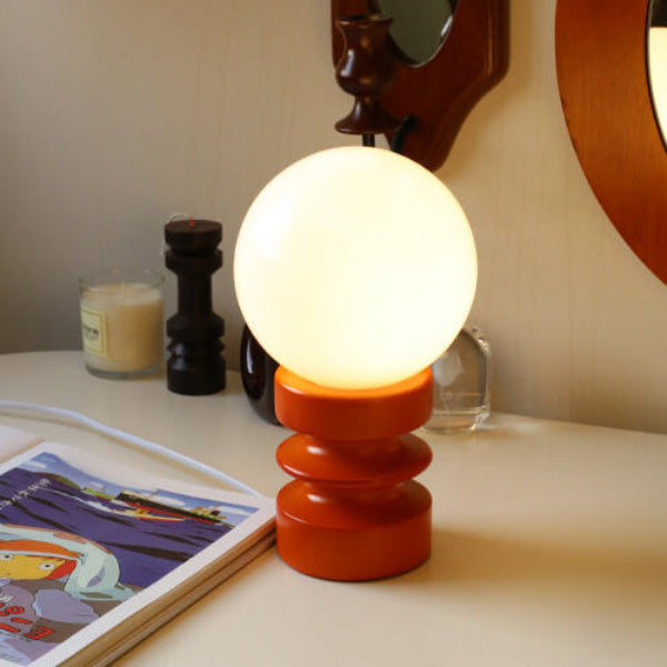 Small table lamp with a round bulb on an orange base on a surface with a magazine and candle.