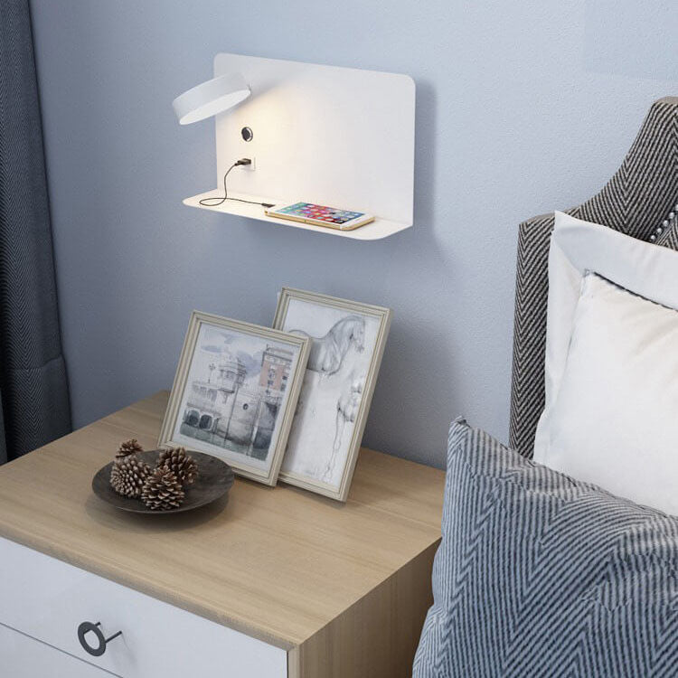 Bedside table with framed pictures, a small lamp, and a bed with pillows.