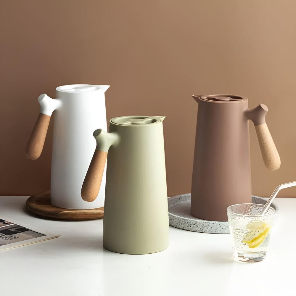 Three ceramic pitchers in white, green, and brown on a table with a glass of water and lemon.
