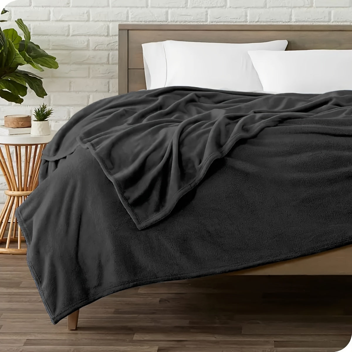 Bed with dark gray comforter and white pillows in a room with a white brick wall and wooden floor.