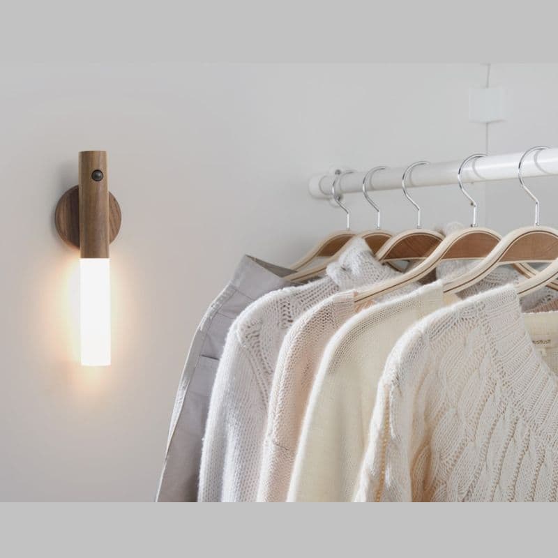 Row of sweaters on wooden hangers with a wall lamp in a minimalistic setting