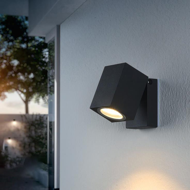 Modern outdoor wall light fixture on a house exterior with a blurred garden background.