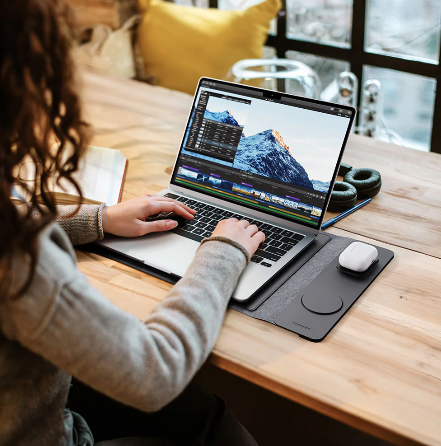 Person using a laptop on a wooden desk with a mountainous landscape displayed on the screen.