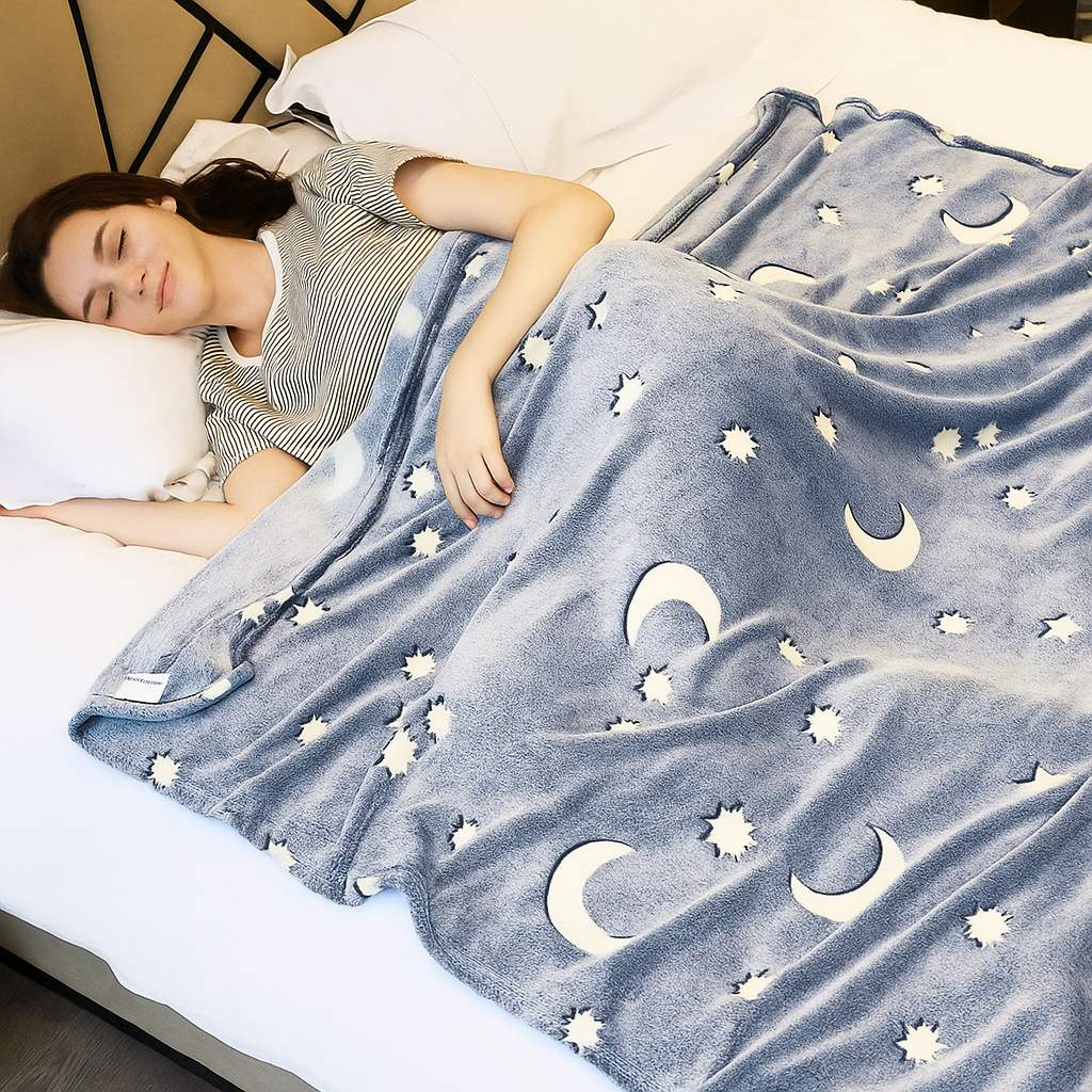 Woman sleeping under a blue blanket with moon and star patterns on a bed.