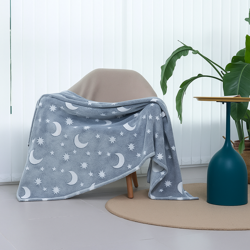 Gray blanket with moon and star pattern draped over a chair in a room with a plant and vase.