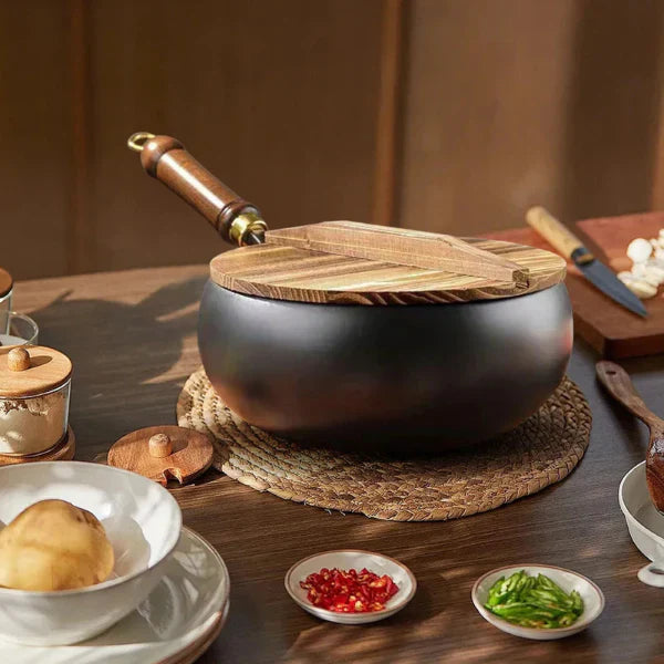 Black pot with wooden lid and spoon on a wooden table with ingredients