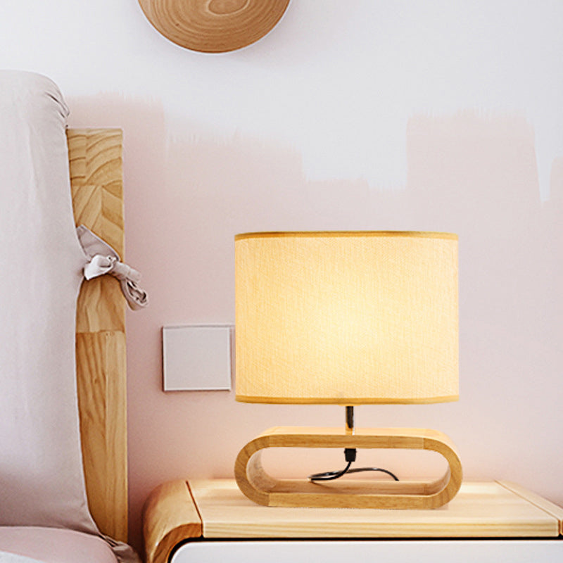 Wooden table lamp with a beige shade on a wooden side table next to a sofa.
