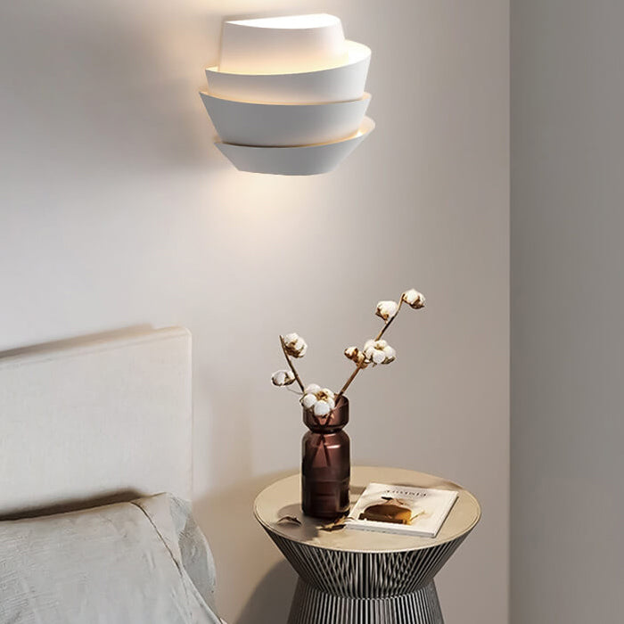 Modern wall-mounted light fixture above a bedside table with decorative elements.