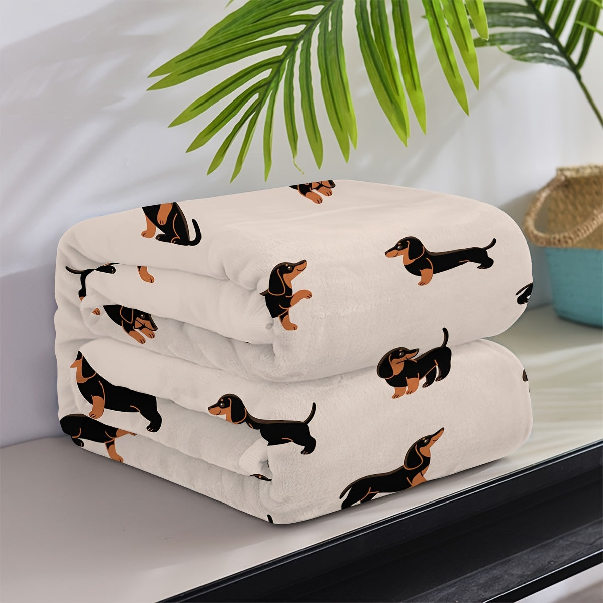 Folded blanket with dachshund pattern on a surface with a plant in the background