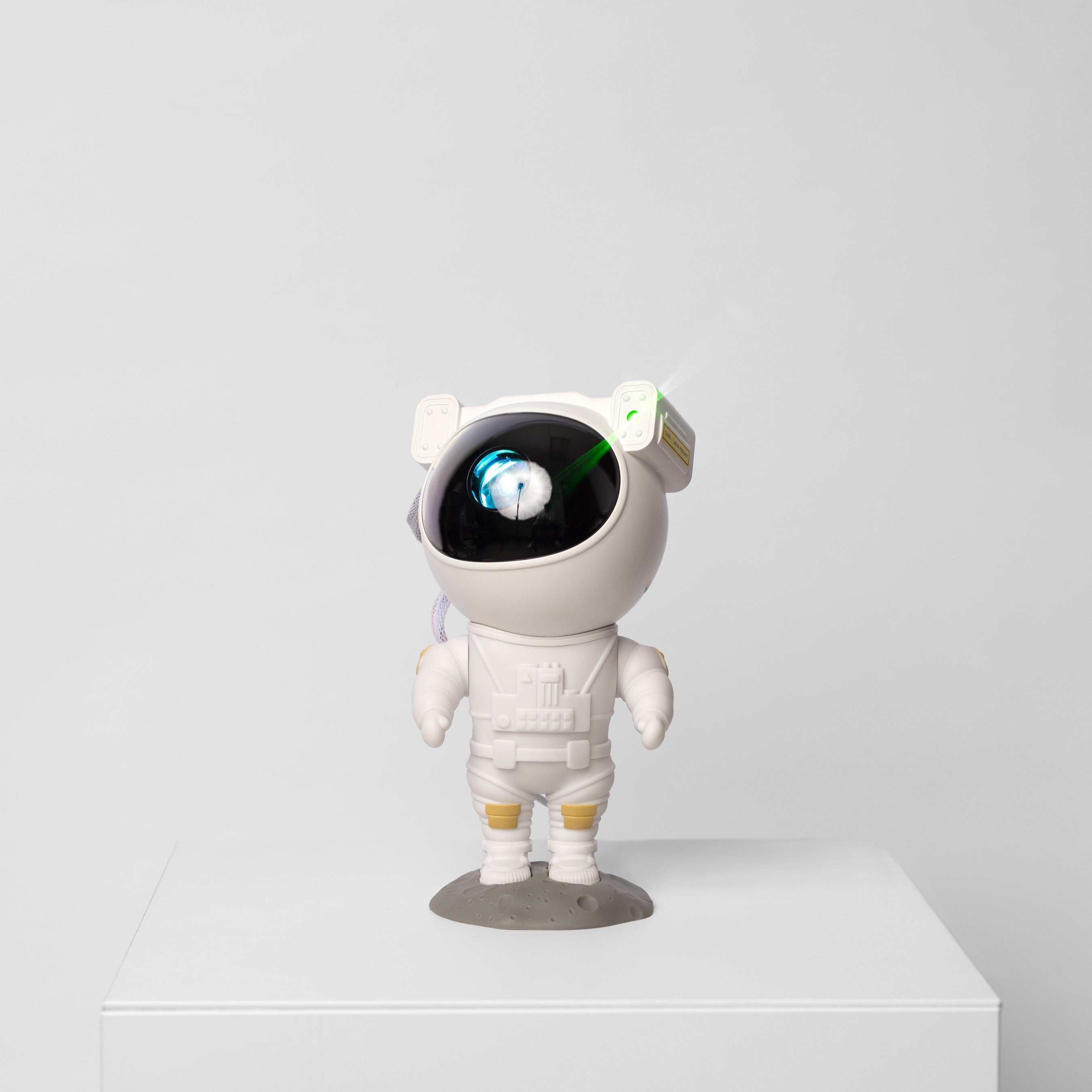 White astronaut figurine with a black face on a white pedestal against a light gray background