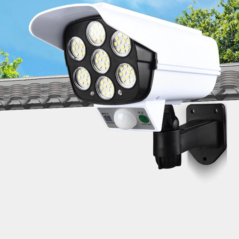 Outdoor security camera with LED lights on a wall, with trees and blue sky in the background.