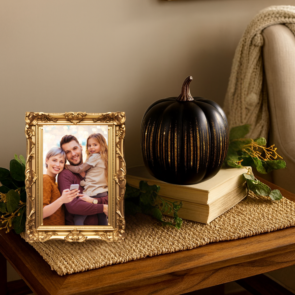 Decorative setup with a gold-framed photo, black pumpkin, and books on a table.